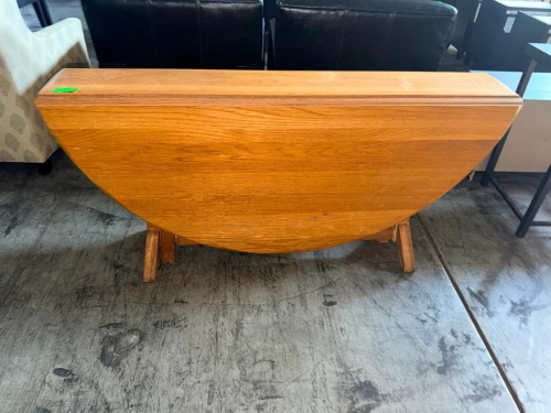 WOOD DROP-LEAF DINING TABLE WITH OAK FINISH, OVAL TOP, DUAL DROP-LEAF DESIGN, PEDESTAL-STYLE SUPPORT STRUCTURE, AND WOOD FEET.