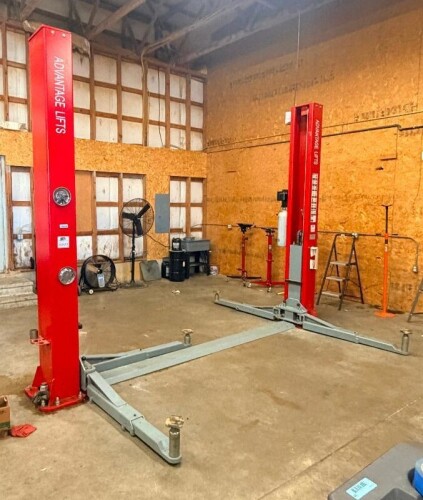 ADVANTAGE LIFTS 12,000 LB. CAPACITY TWO-POST AUTOMOTIVE LIFT WITH HYDRAULIC POWER UNIT, DUAL UPRIGHT COLUMNS, ADJUSTABLE TELESCOPING LIFT ARMS, SWING ARM LIFT PADS, AND FLOOR-MOUNTED BASE PLATES.