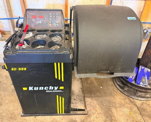 KUNCHY KC-988 AUTOMOTIVE WHEEL BALANCER WITH DIGITAL CONTROL PANEL, AUTOMATIC BALANCING FUNCTIONS, WHEEL GUARD, WHEEL MOUNTING SHAFT, QUICK-RELEASE HUB NUT, WHEEL WEIGHT STORAGE TRAYS, AND ASSORTED WHEEL WEIGHTS AND ACCESSORIES.