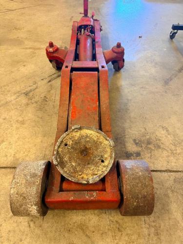 HEAVY DUTY LONG FRAME HYDRAULIC FLOOR JACK WITH MANUAL PUMP HANDLE, STEEL LIFTING SADDLE, DUAL FRONT STEEL WHEELS, AND REAR SWIVEL CASTERS.