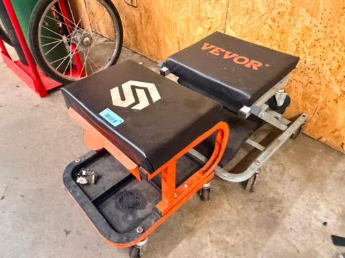 (2) ROLLING MECHANIC'S SHOP STOOLS WITH PADDED VINYL SEATS, STEEL FRAMES, SWIVEL CASTERS, AND LOWER TOOL TRAYS. INCLUDES (1) ORANGE SHOP STOOL AND (1) GRAY VEVOR SHOP STOOL.