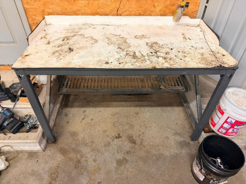 HEAVY DUTY STEEL WORKBENCH WITH WHITE METAL TOP, RAISED BACK AND SIDE EDGES, GRAY STEEL FRAME, AND LOWER SLOTTED METAL STORAGE SHELF. REINFORCED STEEL LEGS WITH CROSS SUPPORTS. TABLES CONTENTS NOT INCLUDED.