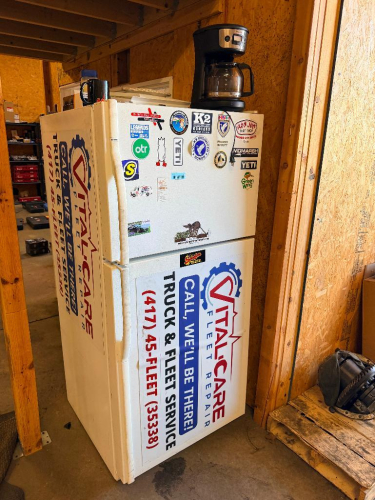 KENMORE COLDSPOT TOP-FREEZER REFRIGERATOR WITH WHITE FINISH, TWO-DOOR DESIGN, FULL-WIDTH REFRIGERATOR AND FREEZER COMPARTMENTS, AND EXTERIOR ADVERTISING DECALS.